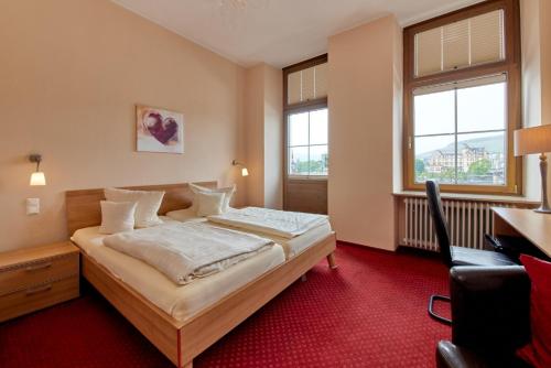 a hotel room with a bed and a desk and windows at Moselhotel Römischer Kaiser in Bernkastel-Kues