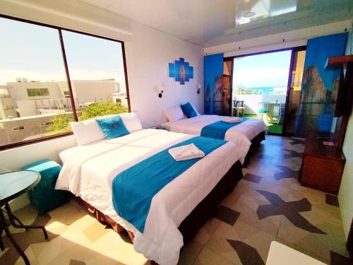 two beds in a room with large windows at Hostal Gosén in Puerto Baquerizo Moreno