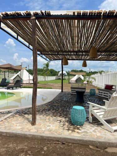 un patio con una sombrilla de madera, un banco y una piscina en Dharma Glamping, en Tapachula
