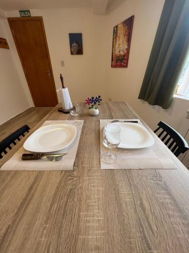 a wooden table with two white plates and wine glasses at Ushuaia_aparts Depto 1 in Ushuaia