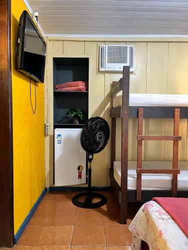a room with a bunk bed with a fan and a refrigerator at Pousada & Camping Tubarão in Ilha do Mel