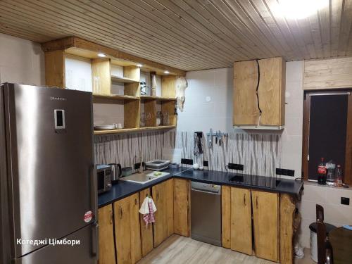 eine Küche mit Holzschränken und einem Kühlschrank aus Edelstahl in der Unterkunft Котеджі Цімбори in Jablunyzja