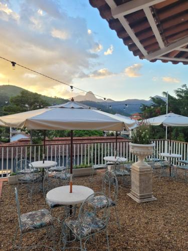 eine Terrasse mit Tischen, Stühlen und einem Sonnenschirm in der Unterkunft La Belle Provence in Itaipava