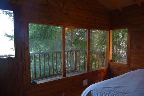 1 dormitorio con 1 cama y ventanas en una casa de madera en Espacio Aquarel Patagonia en El Bolsón