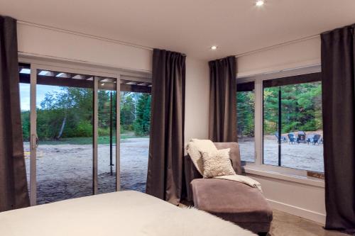 une chambre avec un lit, une chaise et des fenêtres dans l'établissement Le Roselin Exitchalets Spa & Lake, à Notre-Dame-de-la-Merci
