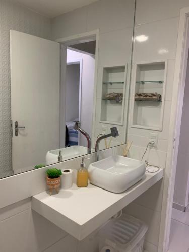 La salle de bains blanche est pourvue d'un lavabo et d'un miroir. dans l'établissement Apartamento Temporada Mobiliado Proximo a Praia, à Vila Velha