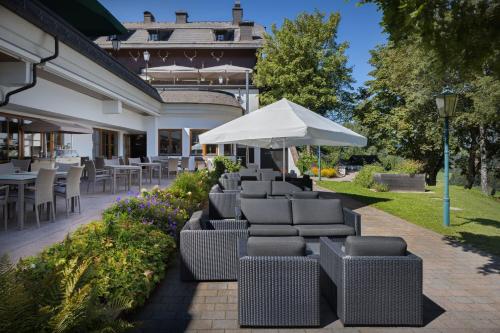 a row of wicker chairs and an umbrella on a patio at Arabella Jagdhof Resort am Fuschlsee, a Tribute Portfolio Hotel in Hof bei Salzburg