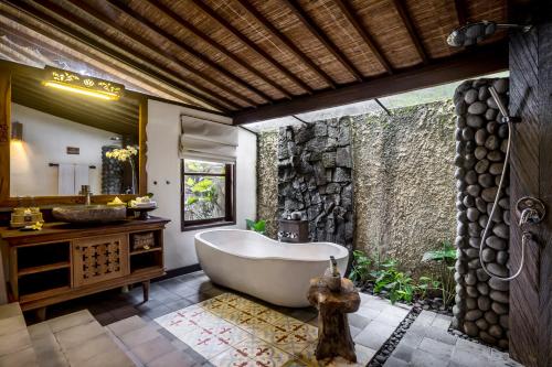 a bathroom with a tub and a stone wall at Pramana Watu Kurung in Ubud