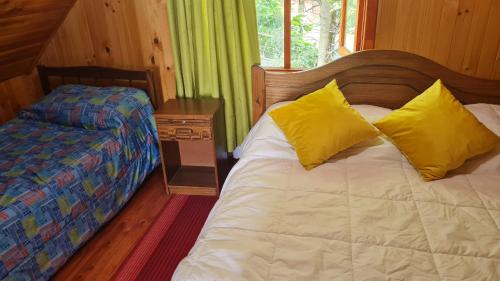 1 dormitorio con 1 cama con 2 almohadas amarillas en Coñaripe Kuyen Mapu Cabañas en Coñaripe