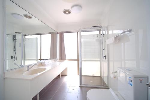 La salle de bains blanche est pourvue d'un lavabo et d'une douche. dans l'établissement Lakeside Inn Wollongong, à Wollongong