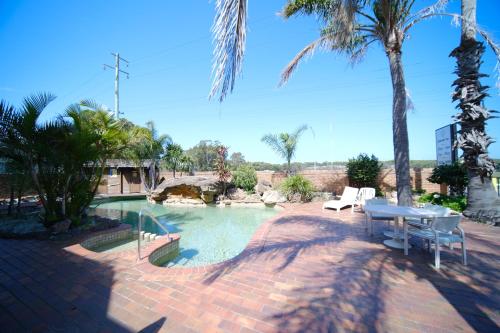 a pool with a table and chairs and palm trees at Lakeside Inn Wollongong in Wollongong