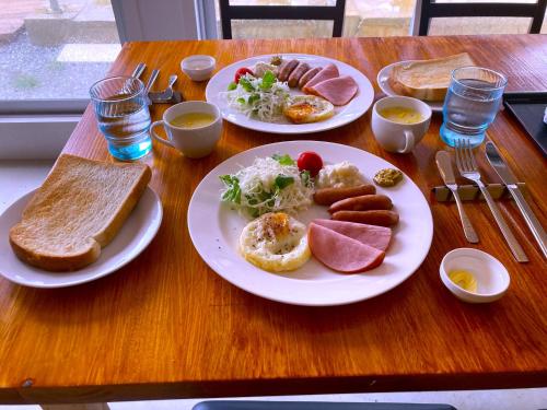 a wooden table with plates of breakfast food on it at Nakijin Resort Guest House in Nakijin