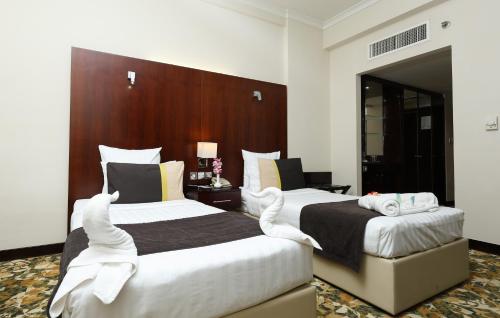 two beds in a hotel room with white sheets at Aavri Hotel in Dubai