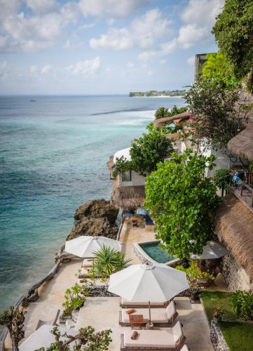 an outdoor swimming pool with umbrellas and the ocean at Rock'n Reef in Uluwatu
