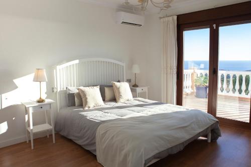 a white bedroom with a bed and a balcony at Villa El Palomar Azul with pool and sea view in Benajarafe