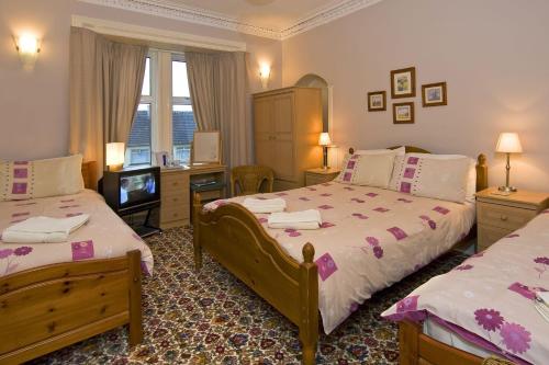 een slaapkamer met 2 bedden, een bureau en een televisie bij St Annes Guest House in Oban