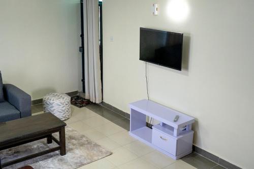 een woonkamer met een bank en een tv aan de muur bij JACARANDA, KAHAWA WEST 2 BEDROOM FULLY FURNISHED in Nairobi