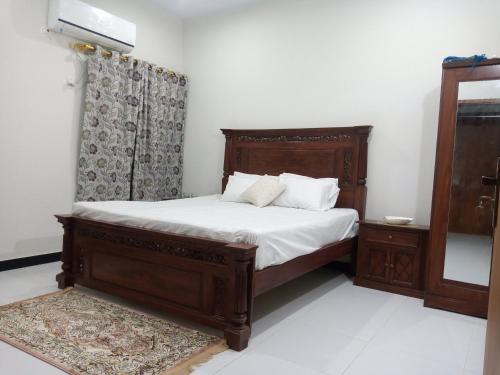 1 dormitorio con cama de madera con sábanas y almohadas blancas en Nursery Inn, en Karachi