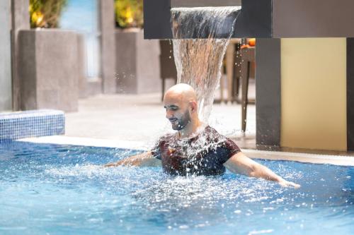 a man in a swimming pool with a fountain at Delta Hotels by Marriott City Center Doha in Doha