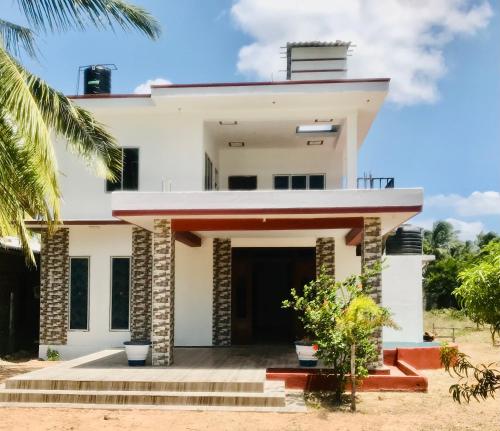 a white house with a front door and palm trees at Villa Moon breeze Nilaveli in Trincomalee