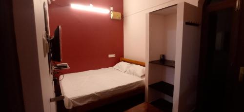 ein kleines Zimmer mit einem kleinen Bett und einer roten Wand in der Unterkunft Siddharth illam in Puducherry