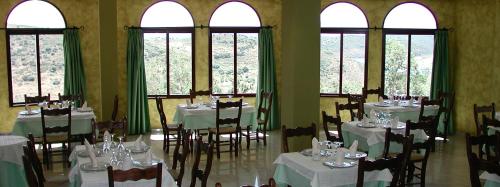 un comedor con mesas y sillas blancas y ventanas en Hotel Restaurante Baños, en Baños de la Encina