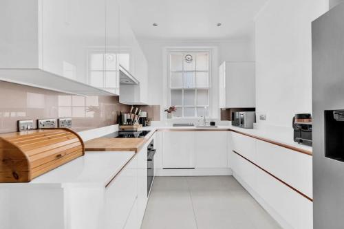 a white kitchen with white cabinets and a wooden counter at Luxury 3 bedroom apartment in the heart of High Street Kensington, London. in London