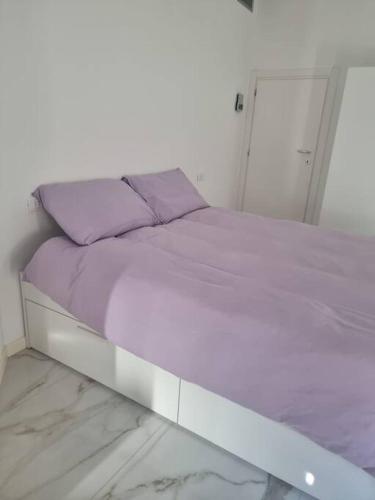 a white bed with purple sheets and pillows on it at Appartamento centro Sondrio in Sondrio