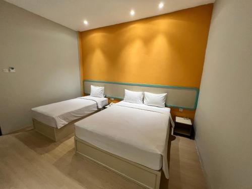 two beds in a room with a yellow wall at Ruma Ruma Hotel Kenten - Palembang in Sukarami