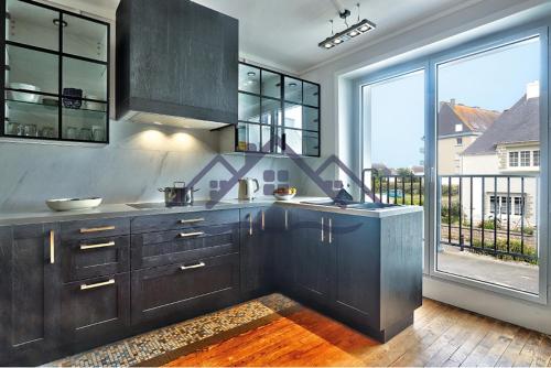 Il comprend une cuisine avec des placards en bois sombre et de grandes fenêtres. dans l'établissement LocaLise - M45 - La grève blanche - Maison avec jardin entièrement clos - A 50m de la plage - Linge de lit inclus - Wifi inclus - animaux non admis, au Guilvinec