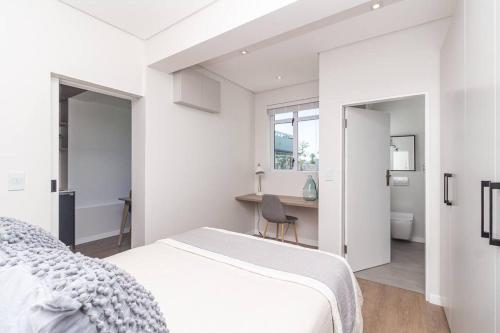 een witte slaapkamer met een bed en een bureau bij Contemporary central apt. Between beach and city. in Kaapstad
