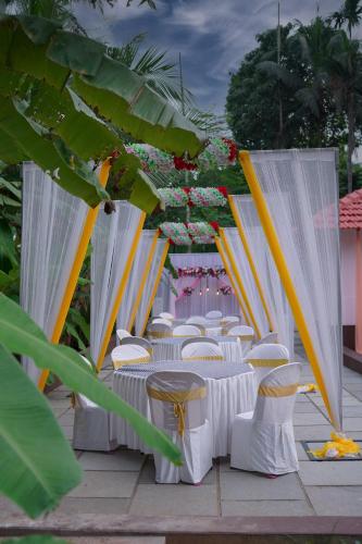 a row of tables and chairs with white curtains at Kaanayi Heritage Home in Payyannūr