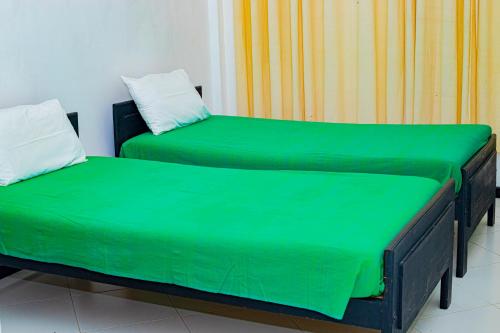two beds with green sheets in a room at Sanasuma Hotel in Hambantota
