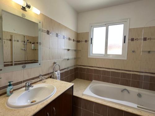 een badkamer met een wastafel, een bad en een raam bij Villa Andy-350 m from the beach in Larnaka