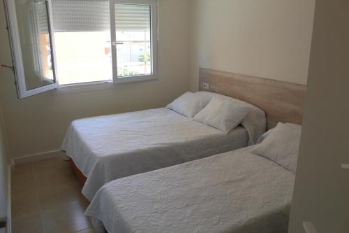 two beds in a small room with a window at Baleares III Apartamento a 100 metros de la arena in Los Mártires