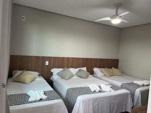 Habitación con 3 camas y sábanas blancas. en Cantinho da Alegria Suítes, en Capitólio