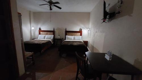 a room with two beds and a table and a ceiling fan at Hotel 19 de Enero Centro in Bernal