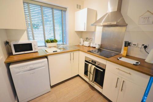 La cuisine est équipée de placards blancs et d'un four avec plaques de cuisson. dans l'établissement Remarkable 3-Bed Ground Floor Apartment - Coventry, à Coventry