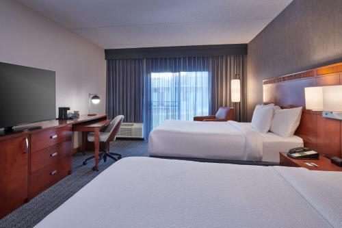 a hotel room with two beds and a desk and a tv at Courtyard Detroit Metro Airport Romulus in Romulus
