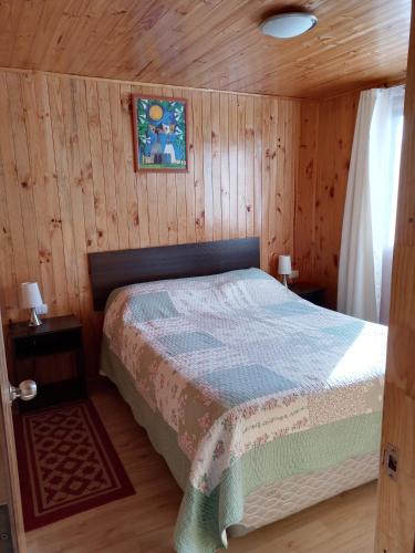 ein Schlafzimmer mit einem Bett in einer Holzhütte in der Unterkunft Cabaña Don Tito en Buchupureo in Cobquecura