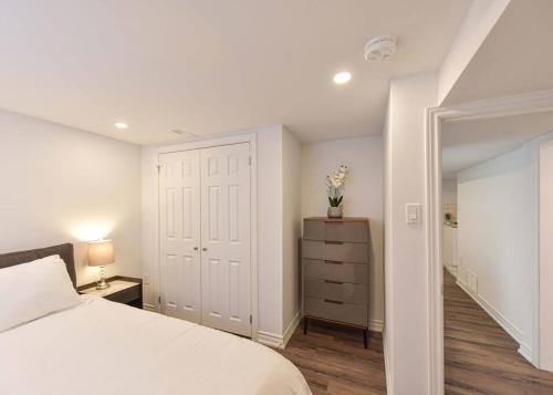 a bedroom with a white bed and a dresser and a closet at Hidden Basement Gem: Cozy Comfort & Outdoor Fun in Barrie
