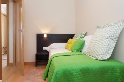 Una cama con almohadas verdes y amarillas. en Aparthotel Jardines de Aristi, en Vitoria-Gasteiz