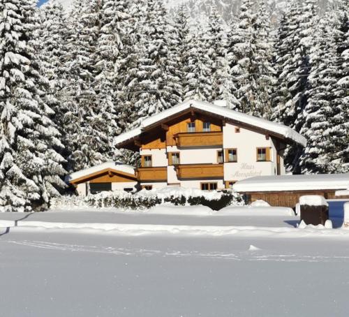a house covered in snow in front of trees at Haus Moosplatzl in Leutasch