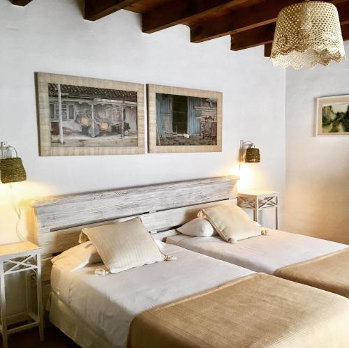 two beds in a room with two lamps and paintings at Cortijo La Viñuela in Atalbéitar