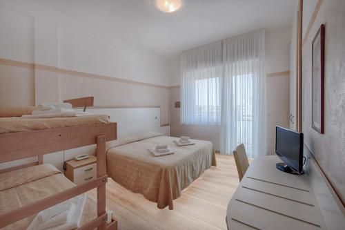 a bedroom with two beds and a desk with a television at Hotel Continental in Milano Marittima