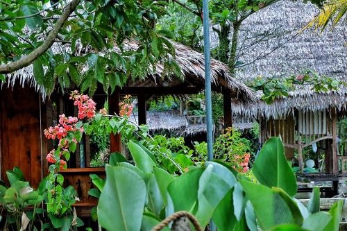 a house with a thatched roof with flowers and plants at Tropical Jungle Hut in Bukit Lawang