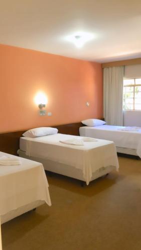 three beds in a room with orange walls at HOTEL VILLA QUATI CENTRO in Foz do Iguaçu