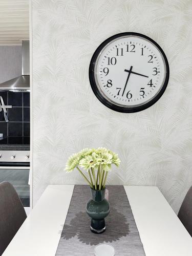 a clock on a wall above a table with a vase of flowers at Ystad Holiday Houses in Ystad
