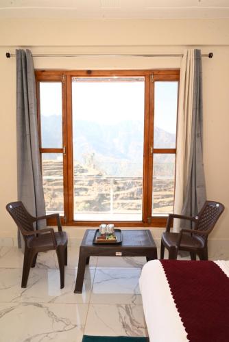 - un salon avec une table, des chaises et une grande fenêtre dans l'établissement Himalayan Hill Top Resort, à Kanatal