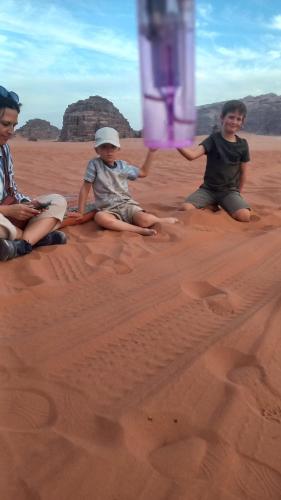 three children sitting on the sand in the desert at غرووب وادي رم in Wadi Rum